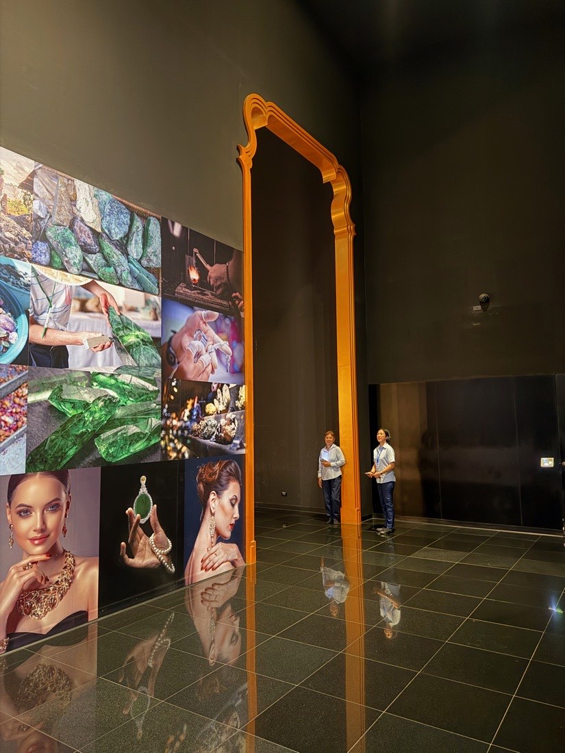 A gilded Thai arch beside a wall-height photographic mural of rough emerald